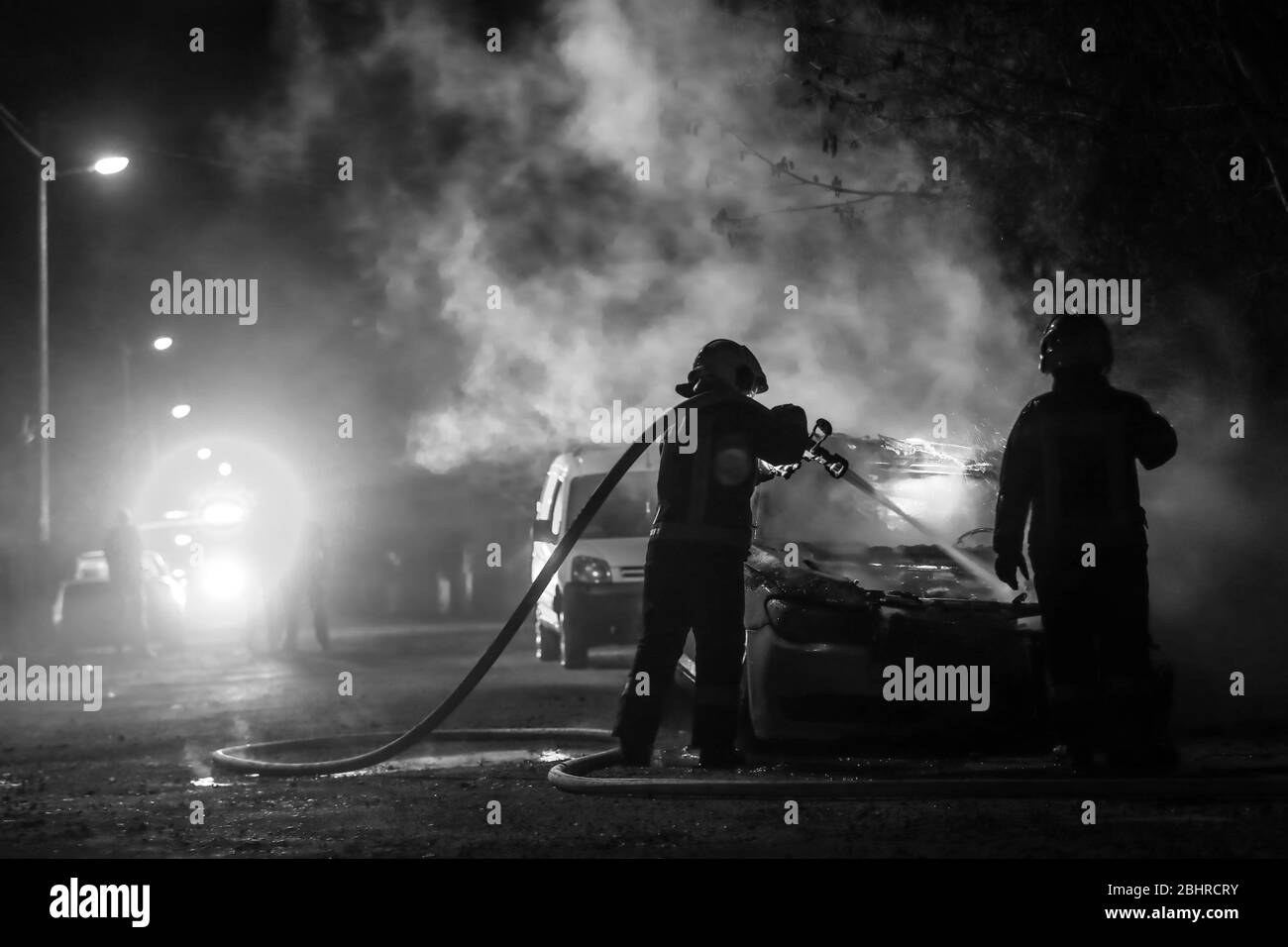 Feuerwehrleute kämpfen gegen das Feuer in der Mitternacht. Polizeiauto in einem Rücken. Schwarz und Weiß Stockfoto