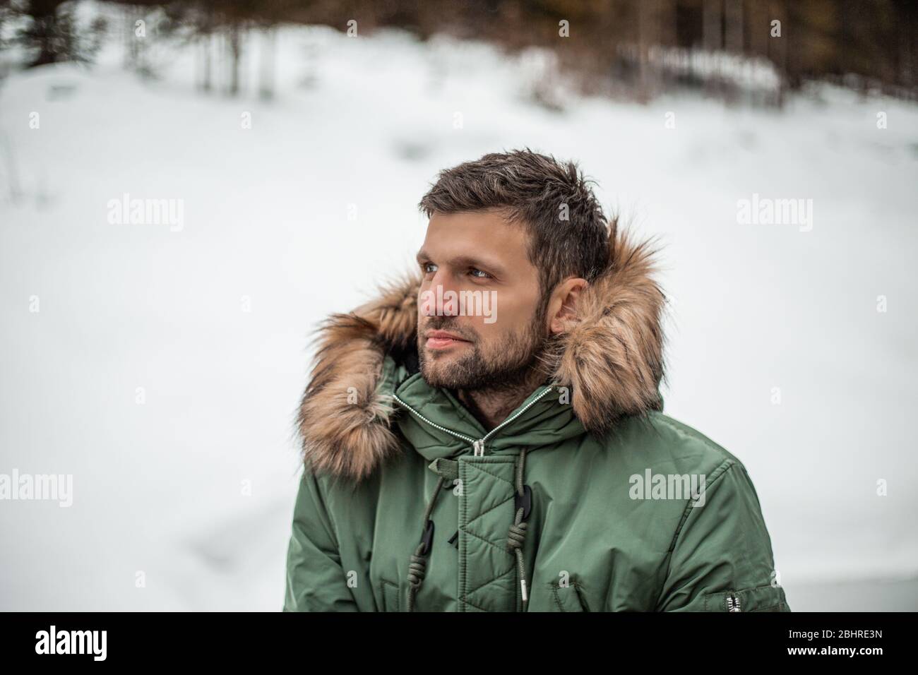 Ein Mann, der einen grünen Mantel mit Pelzbesatz Kapuze trägt, der in einer verschneiten Landschaft steht. Stockfoto