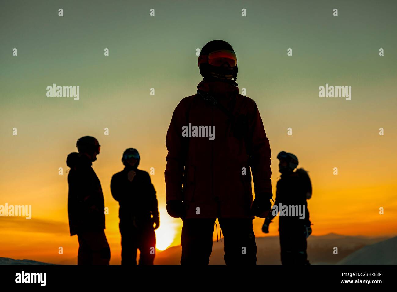 Vier Personen in Skianzügen, Schutzbrillen und Helmen, die gegen den Sonnenuntergang schillerten. Stockfoto
