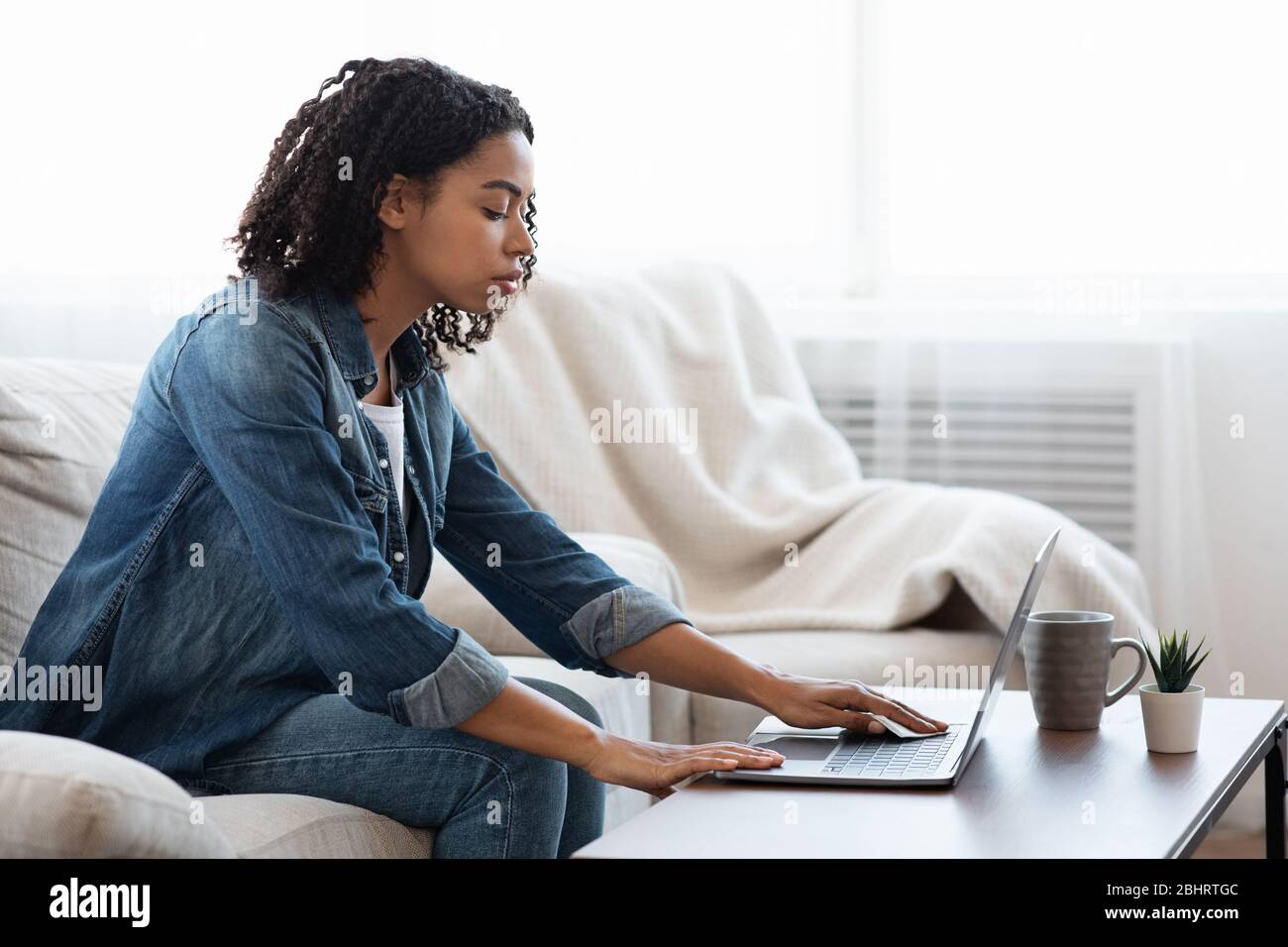 Junge African American Girl Desinfektion Laptop-Tastatur Vor Der Arbeit Zu Hause Stockfoto