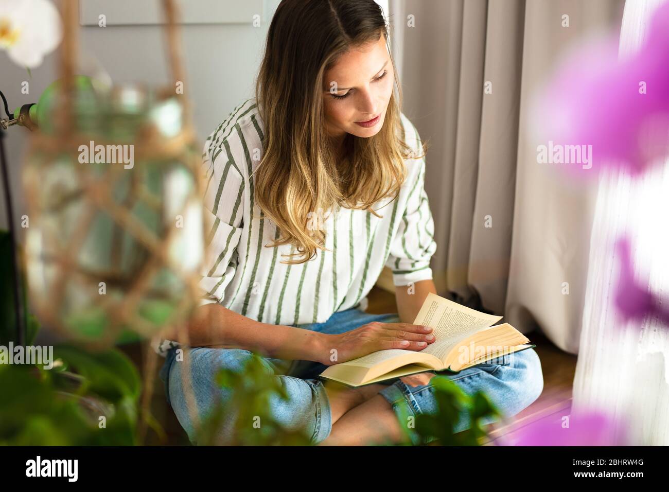 Frau liest neben einem hellen Fenster, entspannt und entspannt während der Ausbruchszeit. Home-Aktivität für einen gesunden Geist Stockfoto