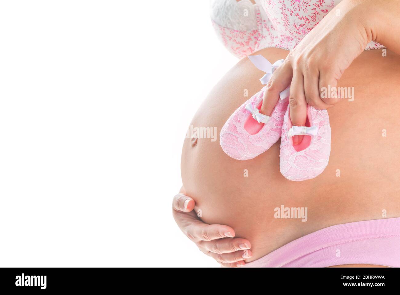 Nahaufnahme Bild der schwangeren Frau mit rosa Babygirl Schuhe auf ihrem Bauch. Isolierter Hintergrund. Mutterschaft pränatale Pflege und Frau Schwangerschaft Konzept. Stockfoto