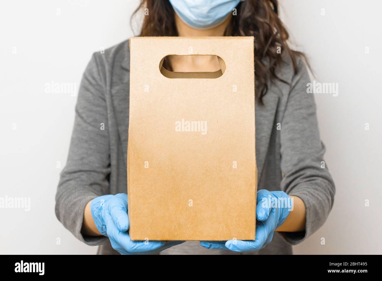 Lieferung Lebensmittelservice während der Quarantäne wegen Coronavirus Ausbruch. Frau mit einer Schachtel in medizinischen Handschuhen und Schutzmaske. Stockfoto