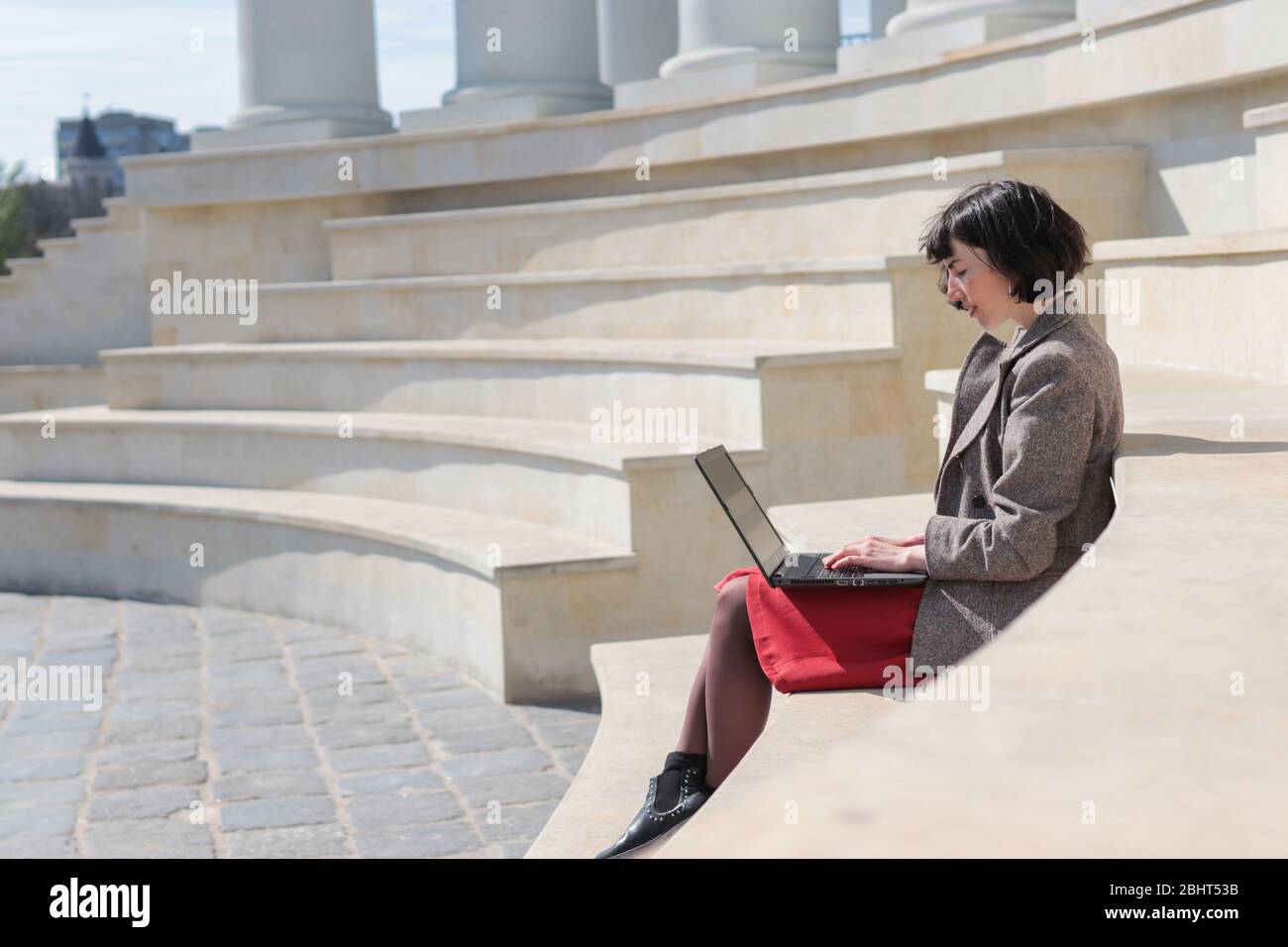 Elegante Geschäftsfrau sitzt auf Stufen, arbeiten auf Laptop, überprüfen und beantworten E-Mails.Technologie, Bildung und Remote-Arbeitskonzept, kopieren Raum Stockfoto