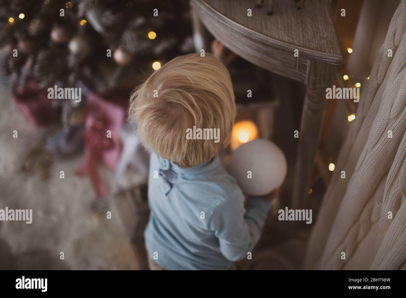 Ein kleiner blonder Junge mit einem Weihnachtsball in den Händen studiert die Welt um ihn herum. Stockfoto