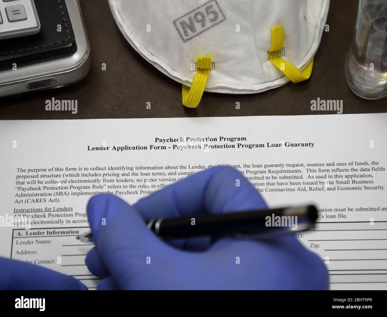 Eine gummihandschuppte Hand ist im Begriff, ein Paycheck Protection Program PPP-Darlehen Formular auszufüllen, das von der US-Regierung Small Business Administration zur Verfügung gestellt wird. Stockfoto