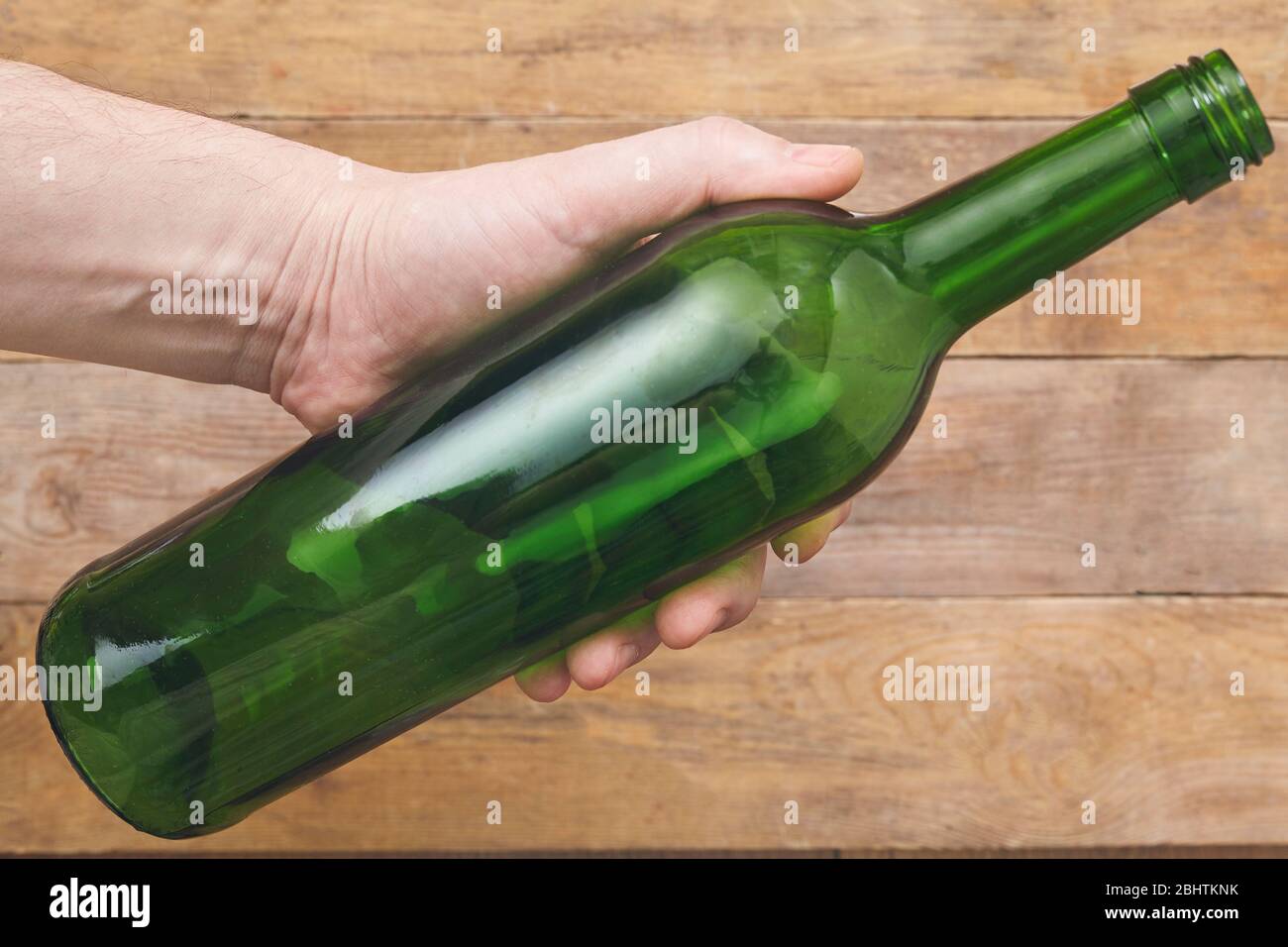 Hand hält eine Weinflasche auf Holzhintergrund. Draufsicht. Stockfoto