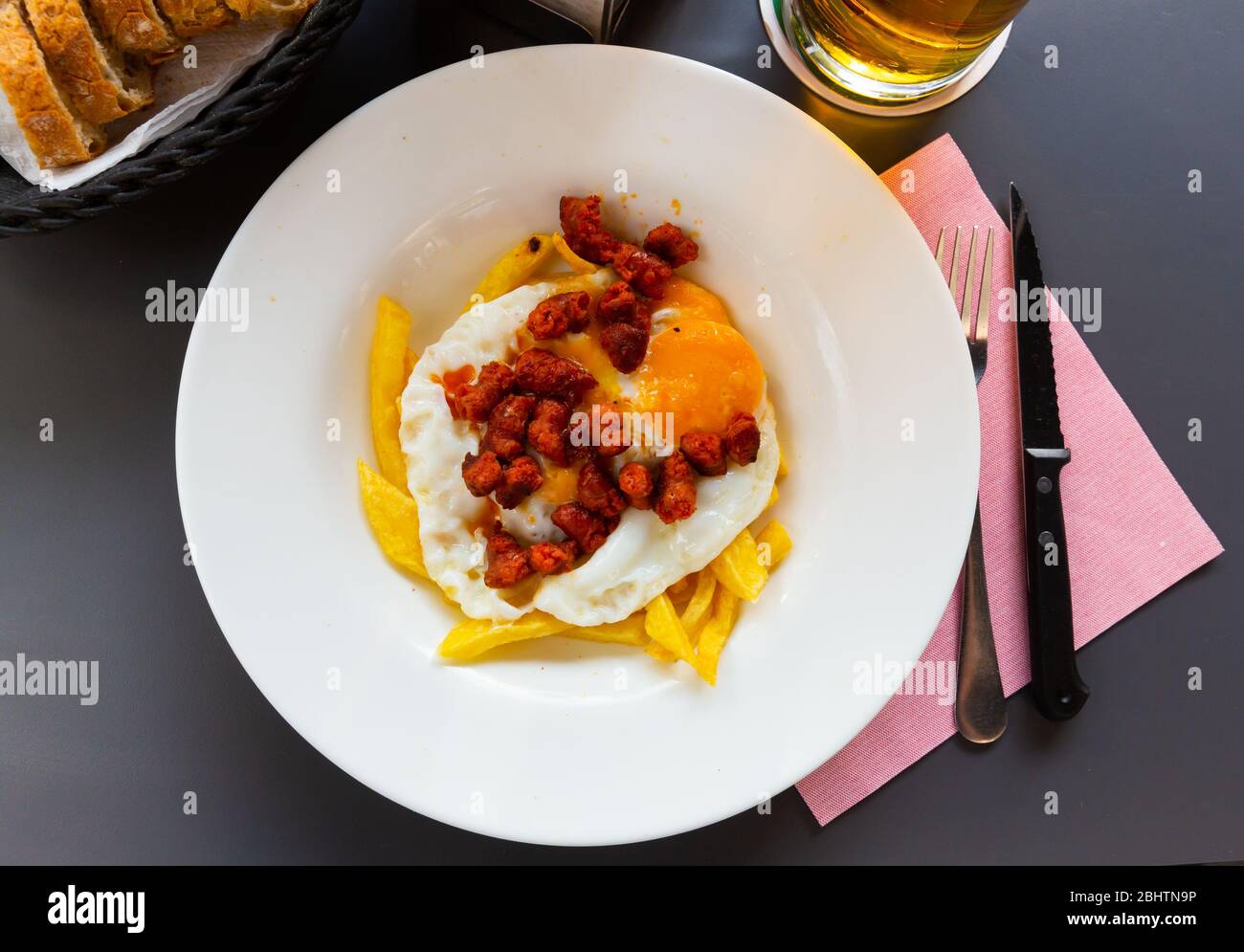 Blick von oben auf das beliebte spanische Gericht mit zerbrochenen Eiern serviert mit gebratenem Chistorra und Kartoffeln Stockfoto