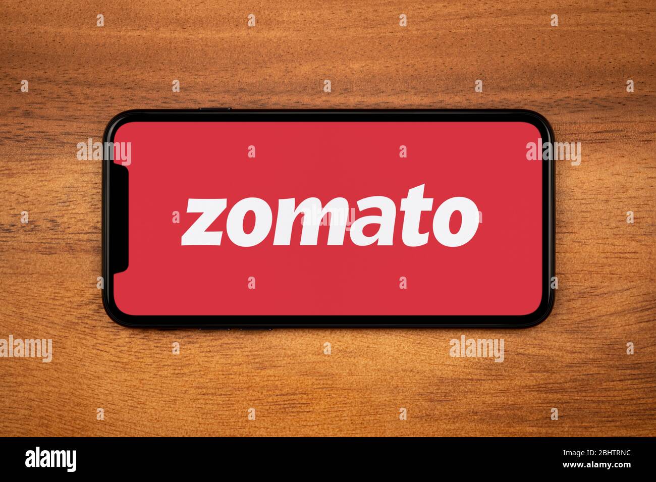 Ein Smartphone mit dem Zomato-Logo liegt auf einem einfachen Holztisch (nur für redaktionelle Verwendung). Stockfoto