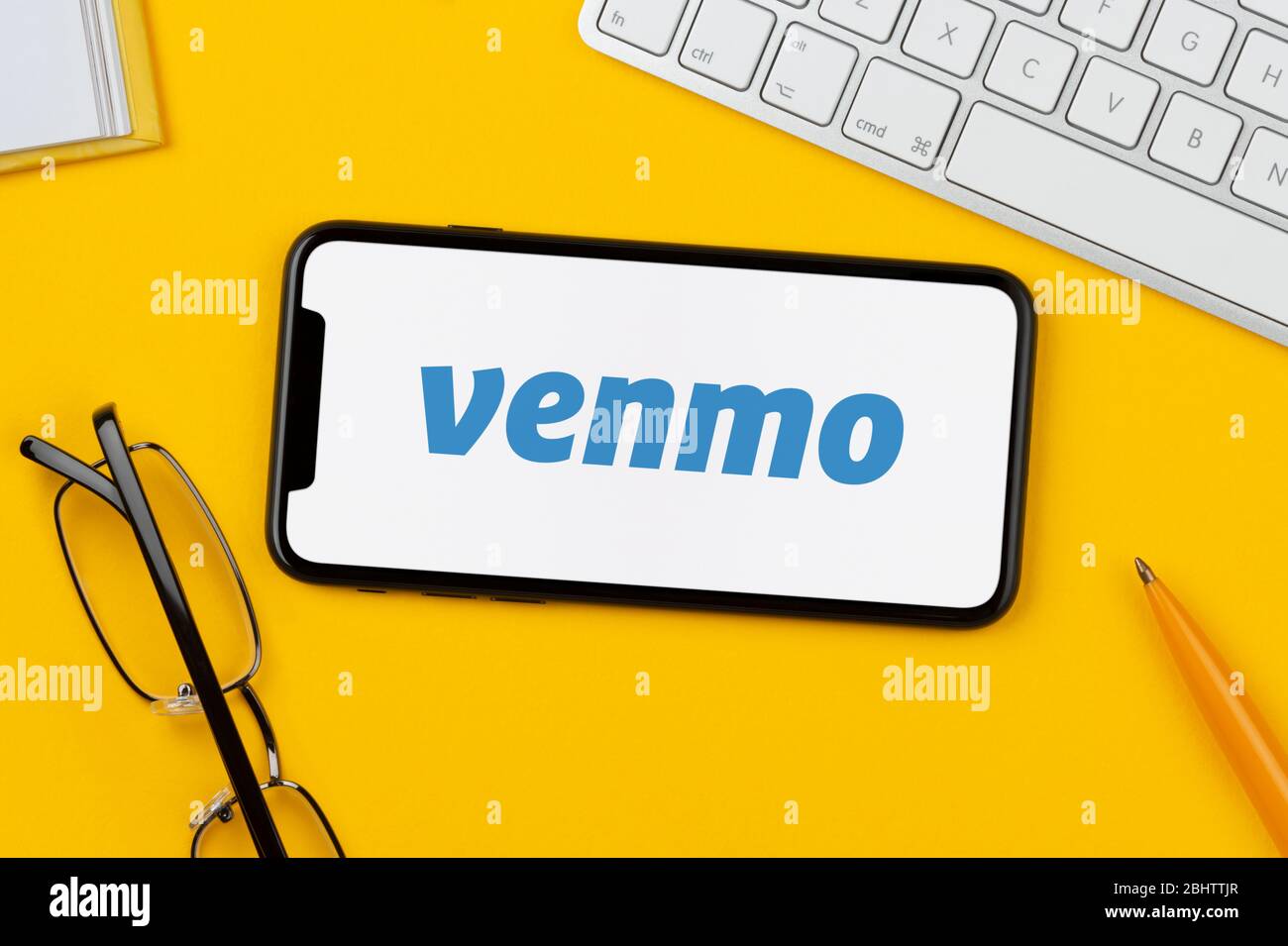 Ein Smartphone mit dem Venmo-Logo liegt auf einem gelben Hintergrund zusammen mit Tastatur, Brille, Stift und Buch (nur für redaktionelle Verwendung). Stockfoto