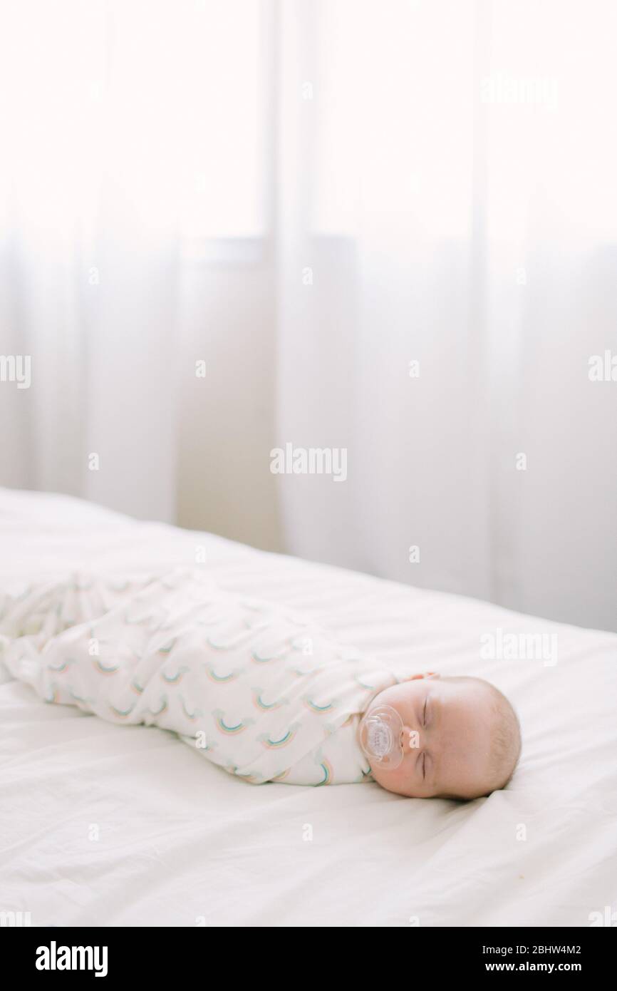 Neugeborenes Schlafen in einer Regenbogendecke auf weißem Bett gebettet Stockfoto