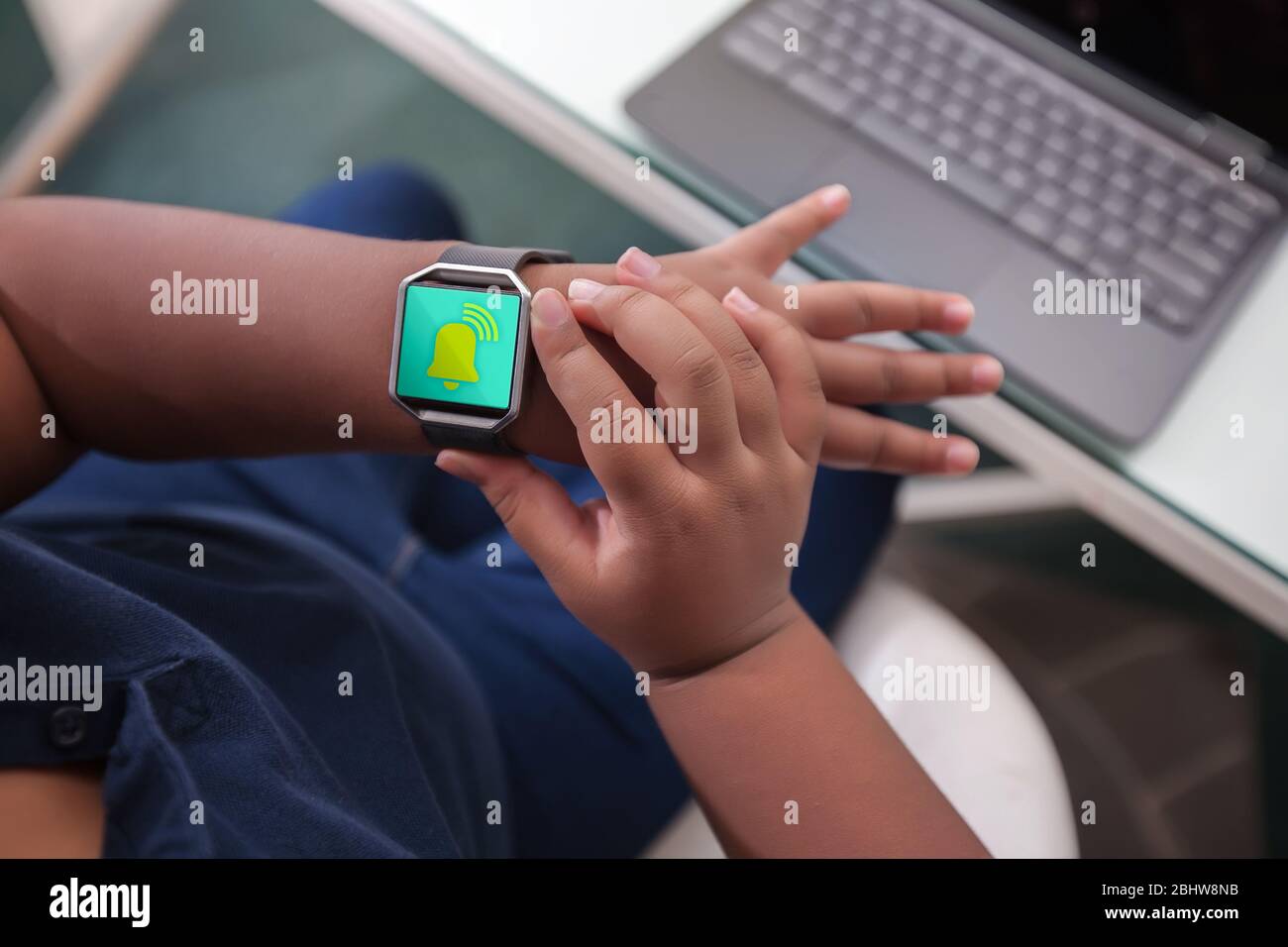 Ein Student sitzt an einem Schreibtisch schaut auf Armbanduhr Alarm zu Tempo und Zeit zu verwalten. Stockfoto