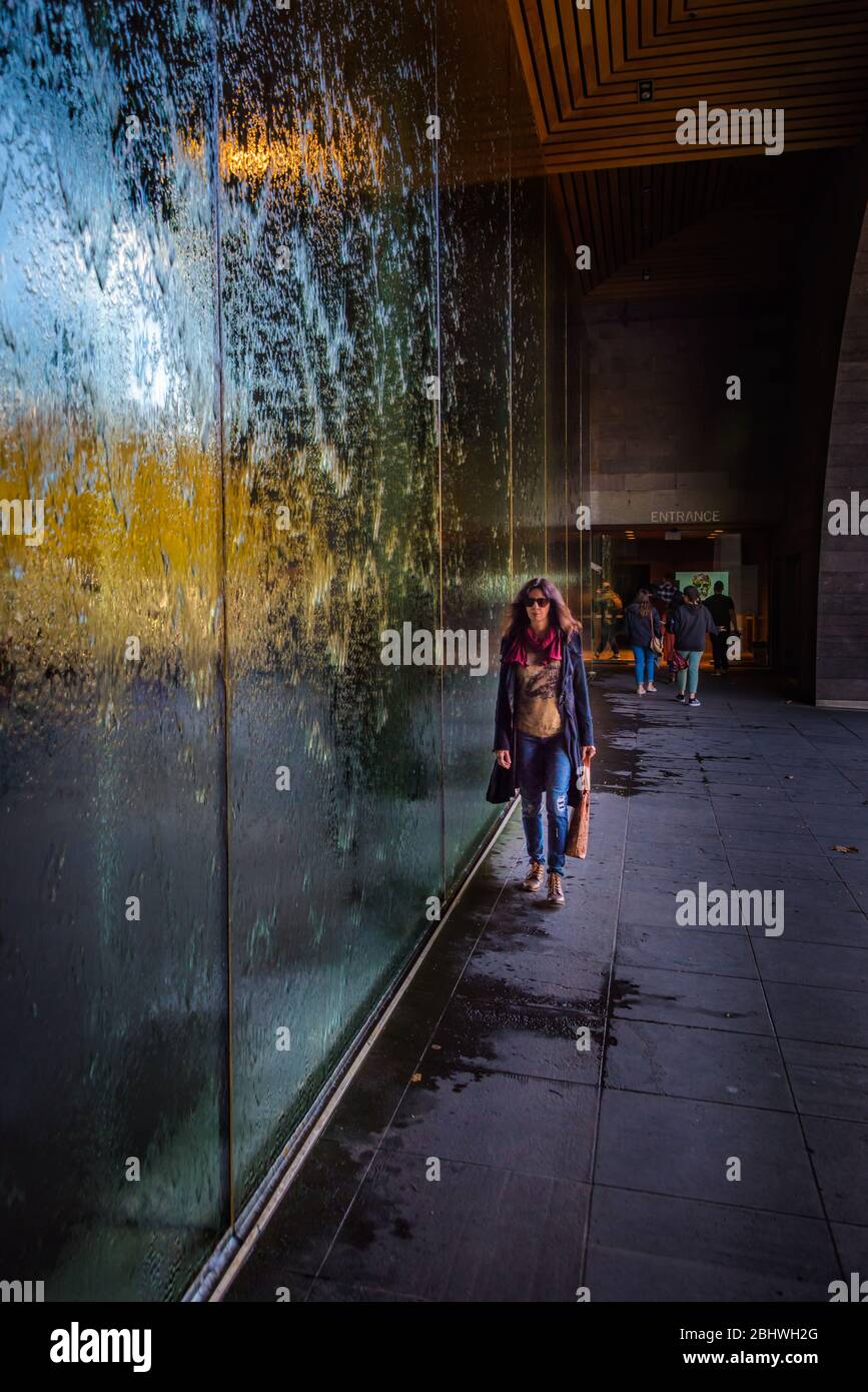 Eine Besucherin spaziert am gläsernen Wasservorhang des Melbourne Arts Museum in Australien entlang. Stockfoto