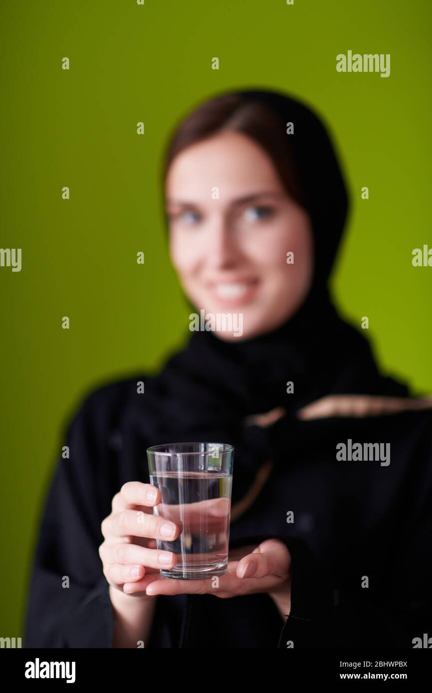 Moderne muslimische Frau in Abaya hält eine Dattefrucht und ein Glas