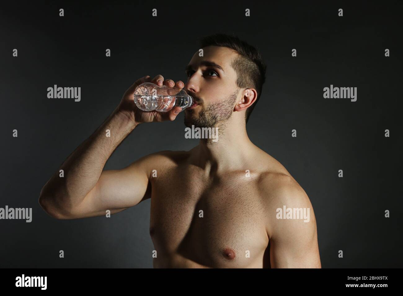 Muskel junger Mann hält Flasche Wasser auf schwarzem Hintergrund Stockfoto