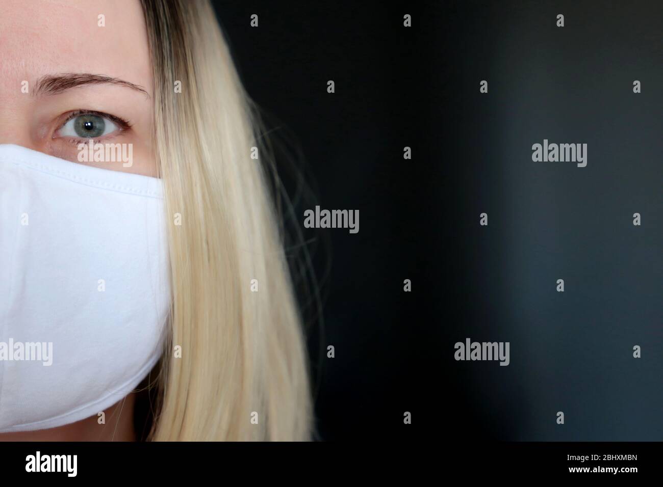 Coronavirus Schutz, blonde Frau in medizinischer Maske auf dunklem Hintergrund, ein halbes Gesichtsporträt. Konzept der Quarantäne während der Covid-19-Pandemie Stockfoto