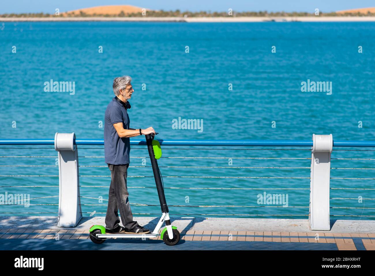 Älterer Mann mit Elektroroller für den Transport am Meer. Gesunde Outdoor Senior Lifestyle Stockfoto