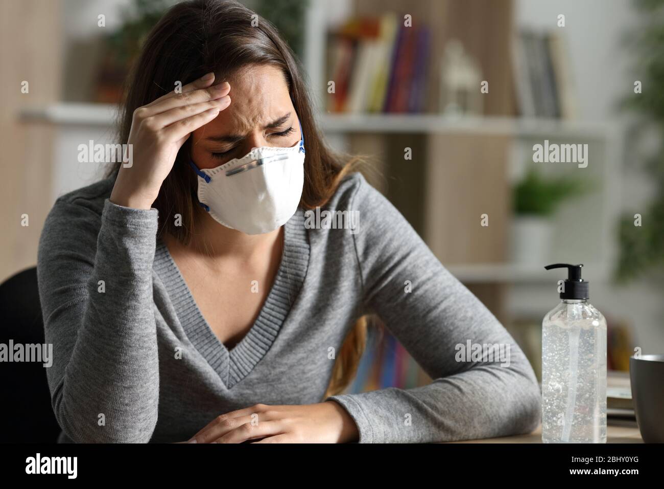 Frau mit Schutzmaske mit Coronavirus-Symptomen, die nachts zu Hause Kopfschmerzen hervorrufen Stockfoto