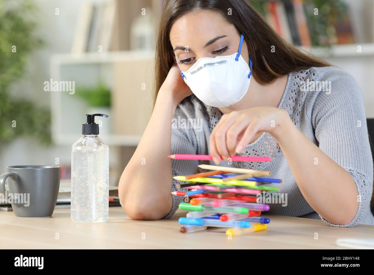 Gelangweilte faule Frau mit Schutzmaske in Quarantänehaft wegen Coronavirus Zeit mit Bleistiften zu Hause spielen verschwenden Stockfoto