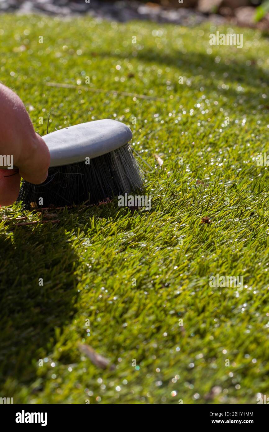 Mann putzt Müll auf Kunstrasen mit einem Handpinsel in der Sonne. Gartenarbeit Konzept Stockfoto