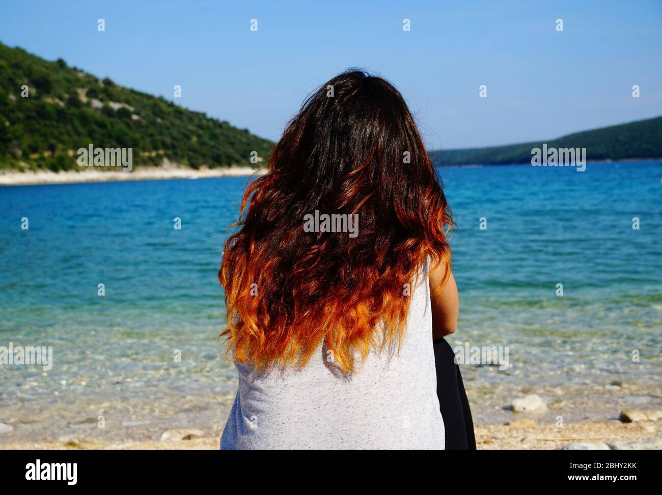 Rothaarige tausendjährige Frau, die in die Ferne über die schöne Seeslandschaft in blau und türkisfarbenen Lagune blickt Stockfoto