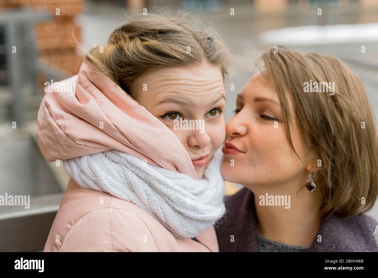 Reife Mutter umarmt und küsst ihre Erwachsene Tochter auf der Stirn, macht das Mädchen Gesichter. Familie Beziehung Konzept Stockfoto