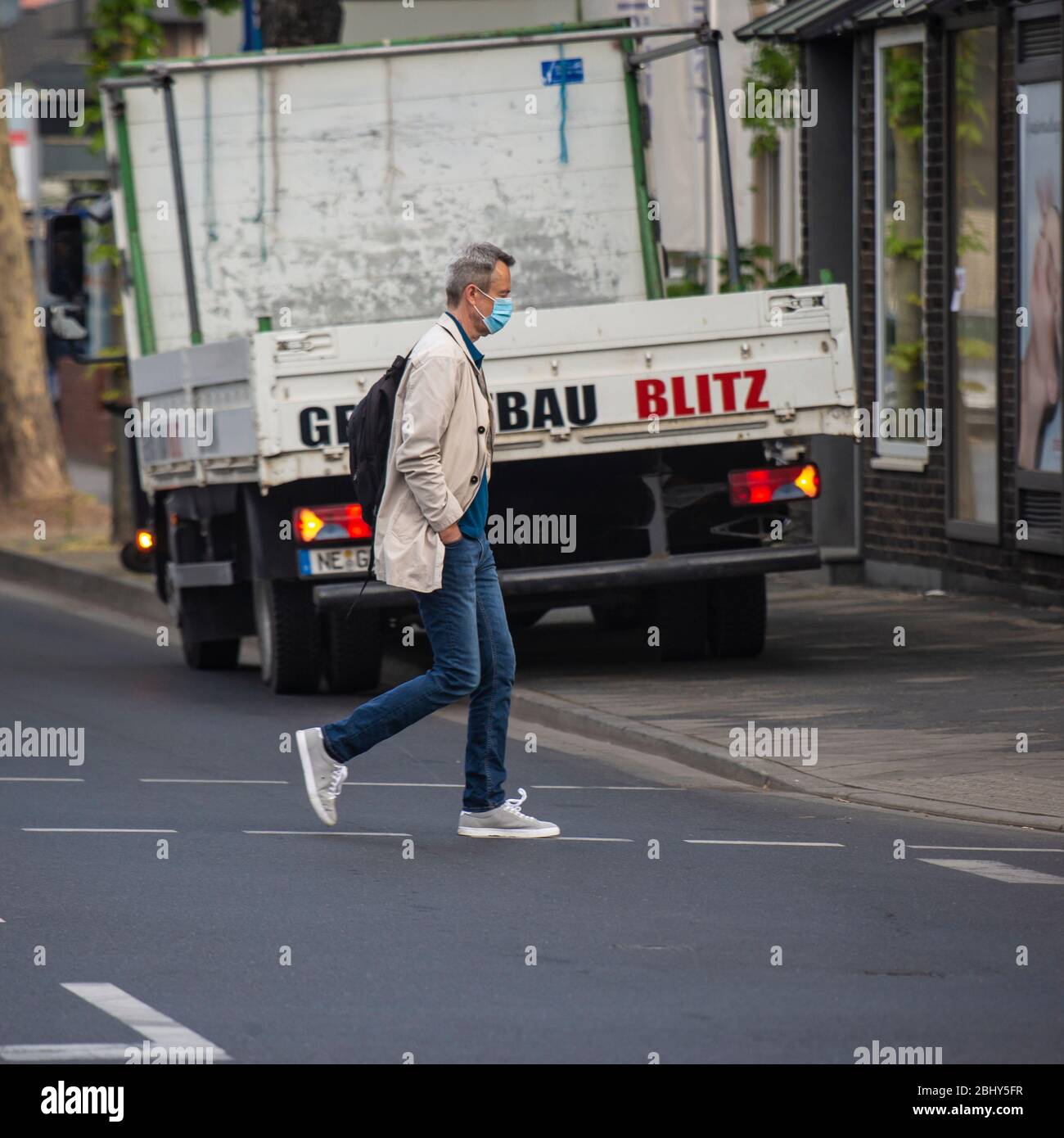 Ein Mann geht in Meerbusch-Büderich über einen Zebrastreifen. Dabei trägt er zum Schutz gegen Corona-Viren eine Mund-Nasen Maske. Diese ist in NRW in Stockfoto