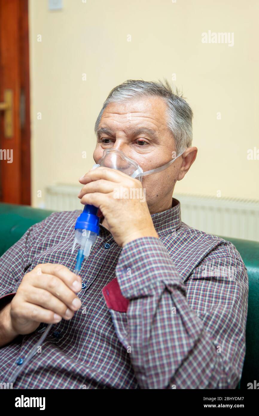 Leitender Mann, der medizinische Geräte für die Inhalation mit Atemschutzmaske verwendet, Vernebler im Zimmer Stockfoto