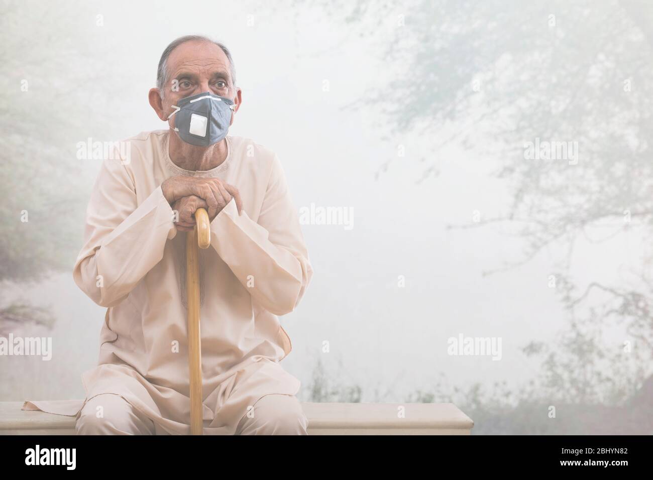 Älterer Mann, der draußen sitzt und eine Umweltmaske trägt. (Gesundheit und Fitness) Stockfoto