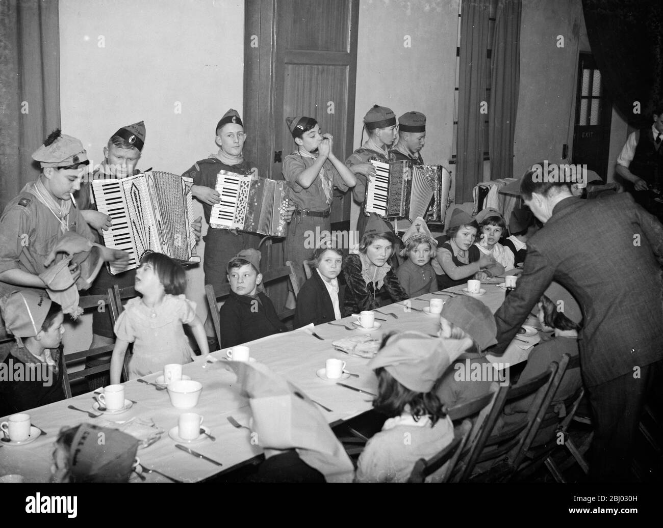 Kinder werden von einer Akkordeonband unterhalten, während sie ihr Weihnachtsfrühstück im Crayford, Kent, genießen. - 1937 Stockfoto