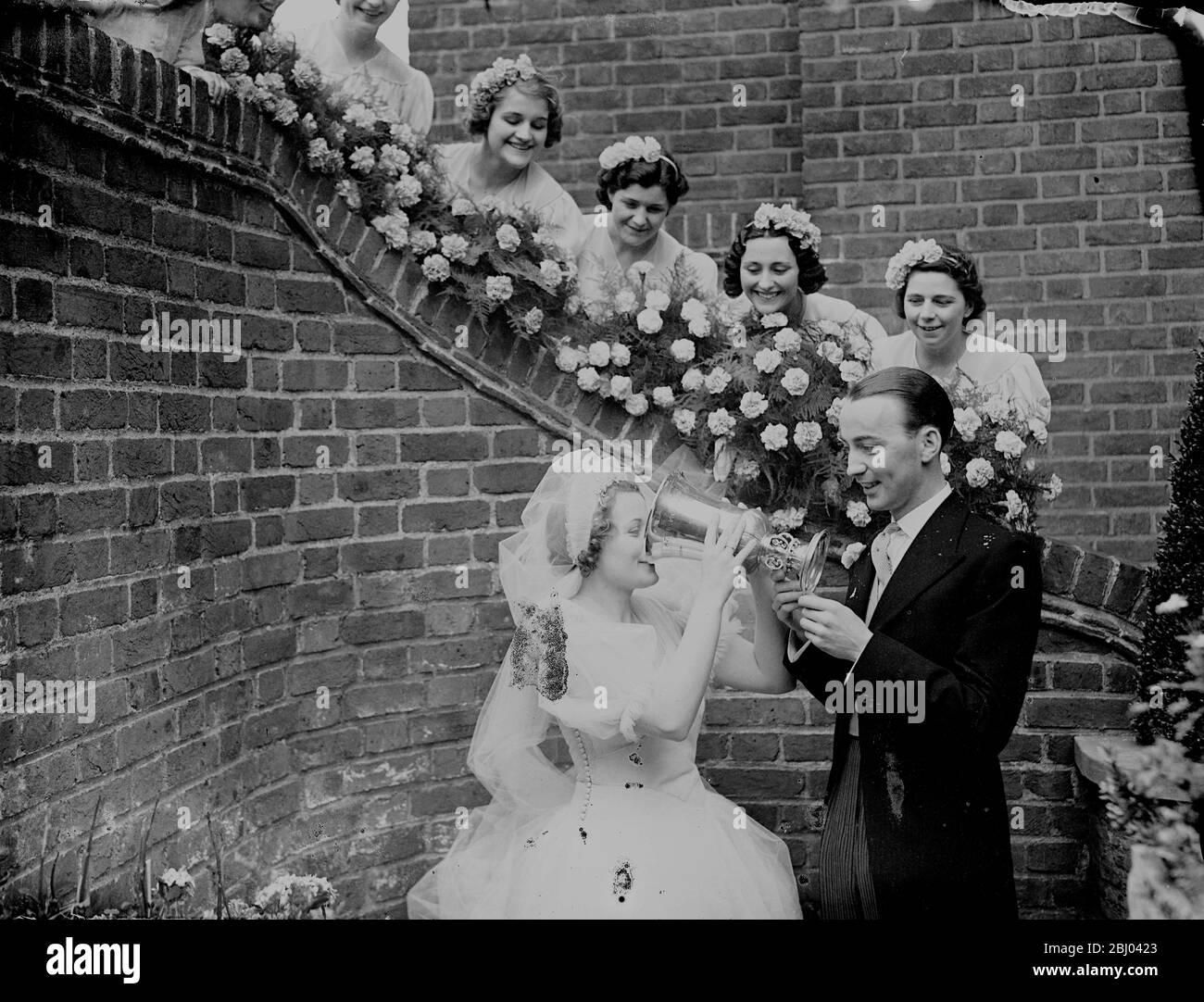 Besitzer des Hundderby Gewinner ist verheiratet in Brompton Oratory. - Herr Jack Walsh, Besitzer von Lane Kiel, Gewinner des Greyhound Derby, wurde in Brompton Oratory mit Miss Ivy Sanders verheiratet. - Herr Alsh hat seiner Braut, Madelast April, versprochen, dass er ihr den Greyhound Derby Cup als Hochzeitsgeschenk überreichen würde. - Foto zeigt, die Braut trinkt einen Toast aus dem Greyhound Derby Cup, gehalten vom Bräutigam, und beobachtet von den Brautjungfern bei der Hochzeitsfeier. - 3. Juli 1938 Stockfoto