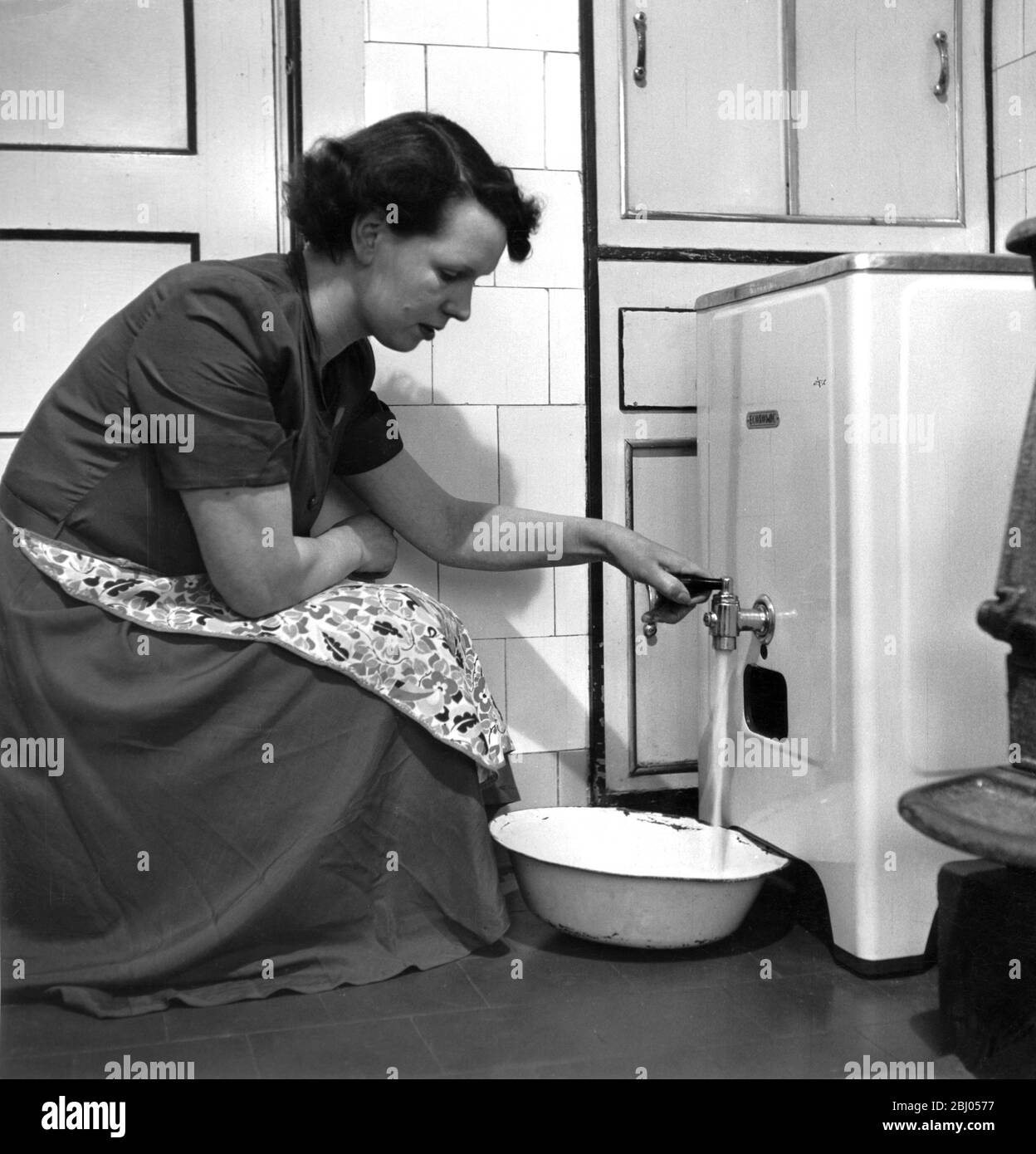 Mutter in der Küche, die heißes Wasser aus ihrem Gasboiler in eine Schüssel zieht.1953 Stockfoto