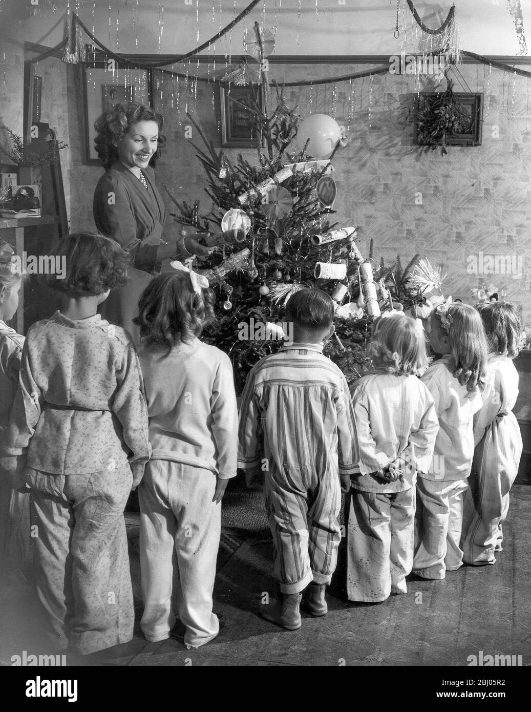 Kinder Schlange neben dem Weihnachtsbaum, um einen Cracker zu erhalten. - 25. Dezember 1947 Stockfoto