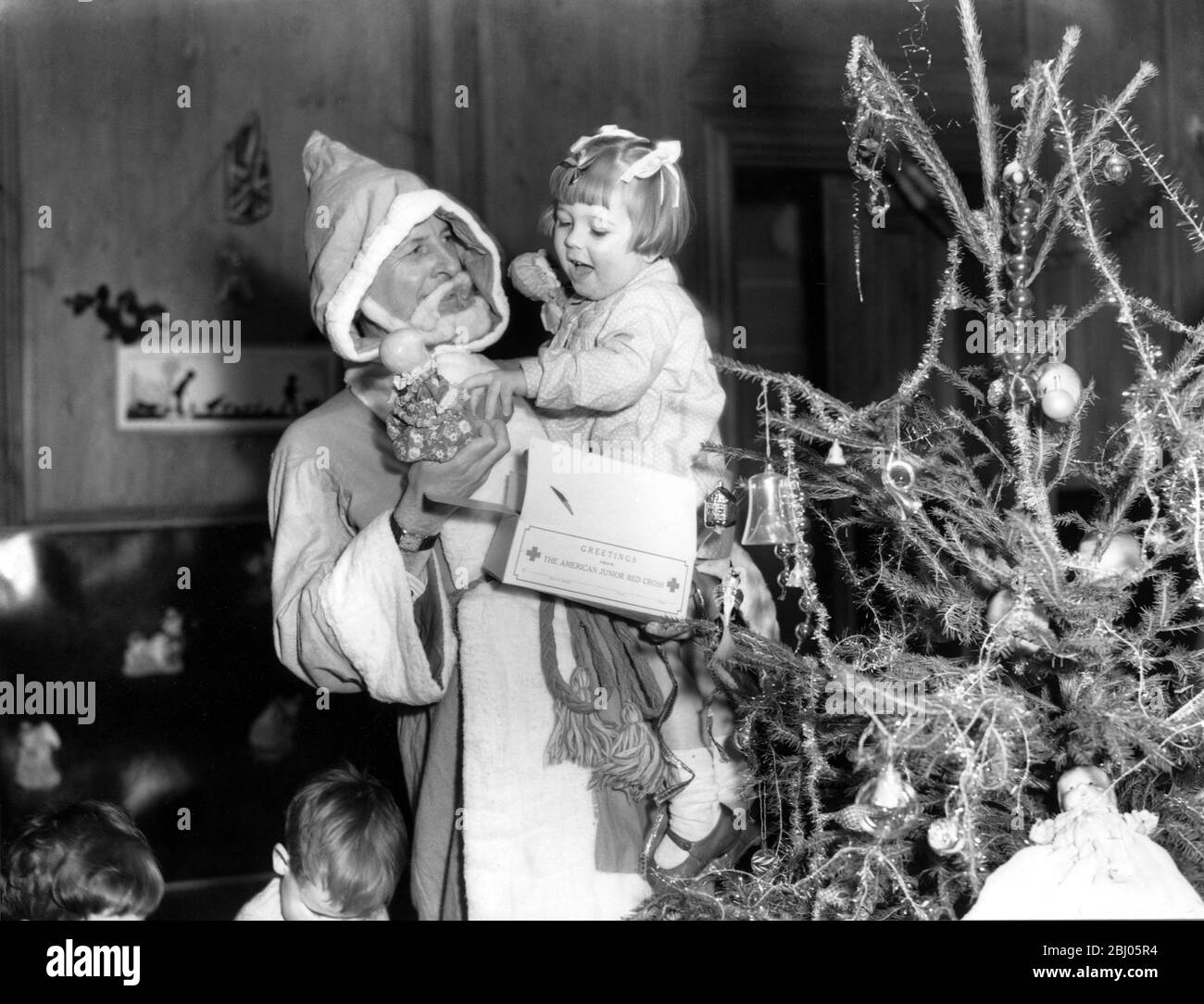 Weihnachtsjubel aus Amerika für bombardierte und evakuierte Londoner Kinder. Kinder im WVS Nursery in der Hanover Lodge, Regent's Park, die darauf warten, in Kindergärten im Land evakuiert zu werden, erhielten ihre Weihnachtsgeschenke auf einer Party, auf der Bernard Carter, der Delegierte des amerikanischen Roten Kreuzes in Großbritannien, als Weihnachtsmann fungierte. Bernard Carter mit einem glücklichen kleinen Mädchen, nachdem sie ihr Geschenk erhalten hatte. - 20. Dezember 1941 Stockfoto