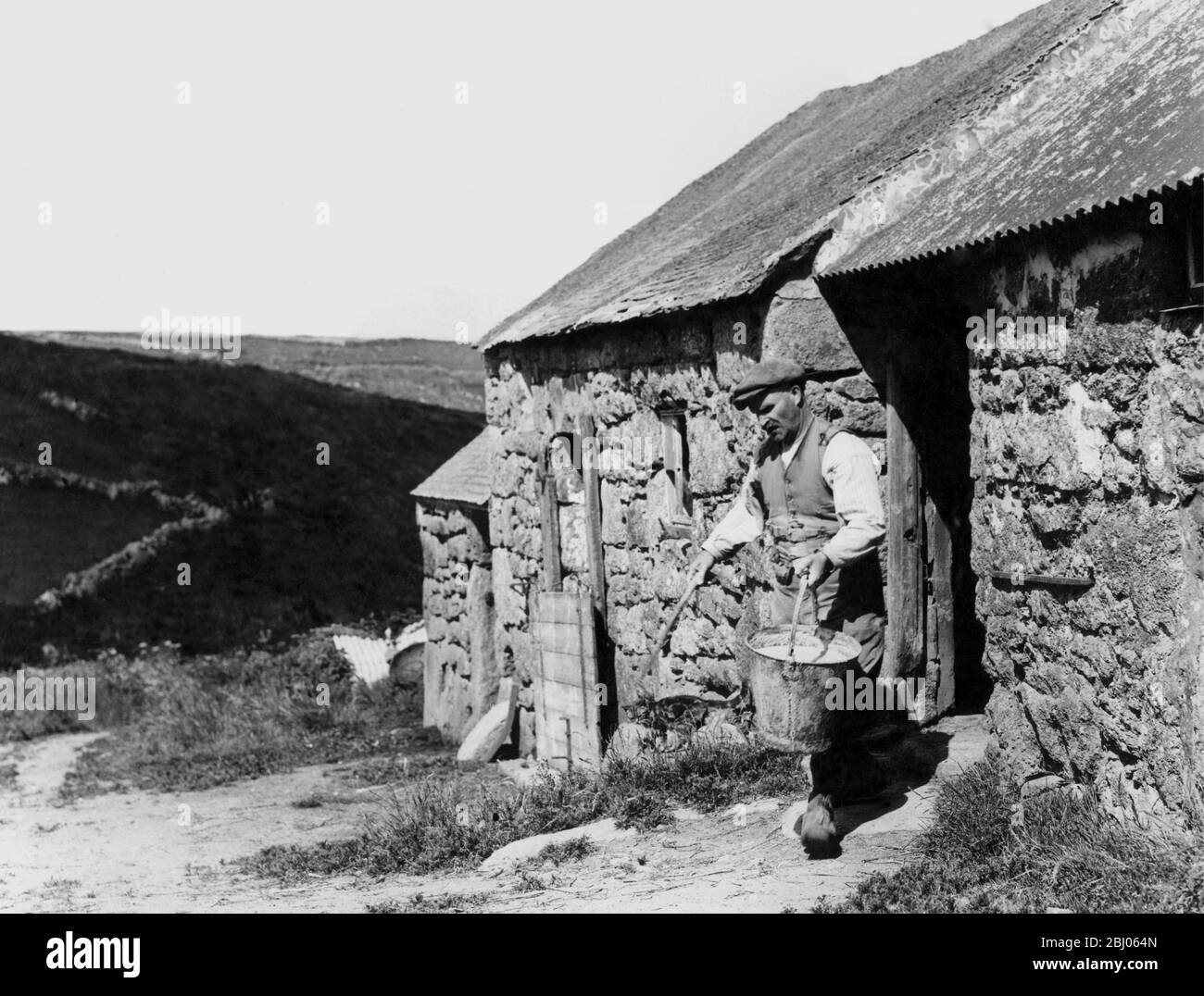 Ein Hügelbauer, der einen Eimer Schweineblauch herausbringt, Cornwall 1936. - die dreißiger Jahre waren eine schlechte Zeit für die englische Agrarkultur; viele Schriftsteller kommentierten das heruntergefallene Gebäude und verfallene, von Unkraut befallene Felder. Stockfoto