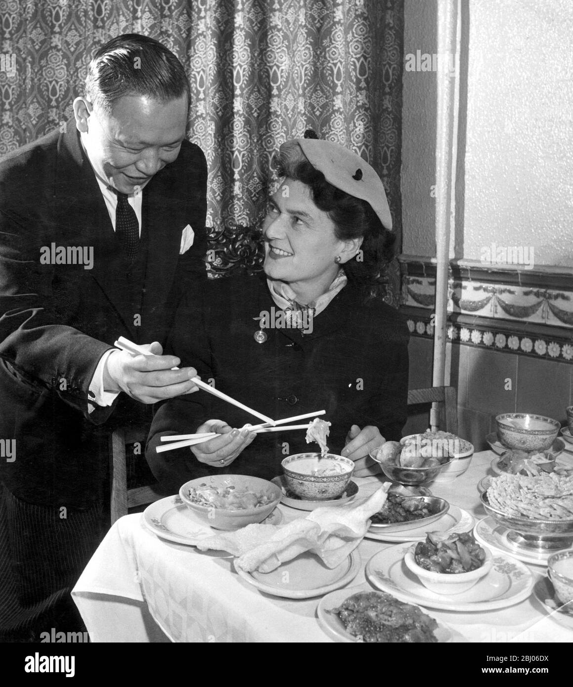Frau Olga Noble-Matthews lernt, wie man Essstäbchen mit Hilfe von Manager Mr Young vom Hong Kong Restaurant in London benutzt.1952 Stockfoto