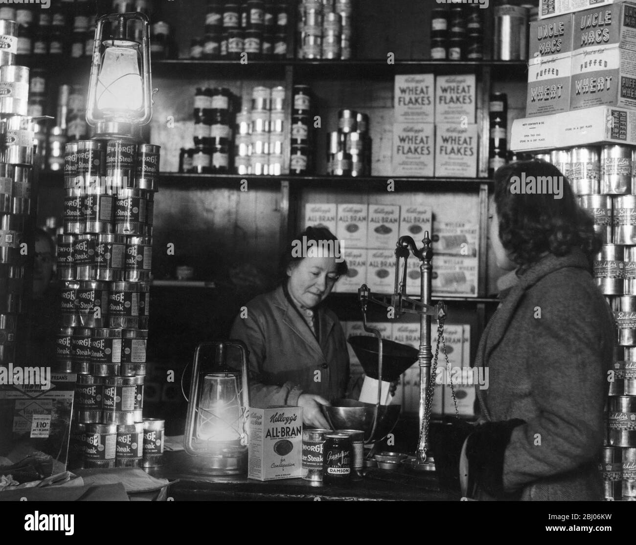 Kraftstoffkrise von 1947: - Londoner Büros und Geschäfte, als die Lichter als Folge der Stromausfälle ausgingen, mit unterschiedlichen Arten der Beleuchtung weitergeführt. Foto zeigt Shopping im Licht von Hurrikan-Lampen in einem Lebensmittelgeschäft in Blackfriars, London. E.C. am 10. Februar 1947. - Stockfoto