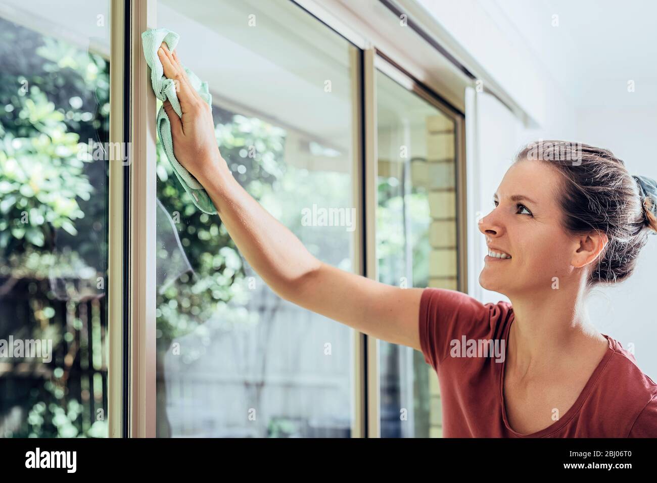 Junge lächelnde Frau putzt Fenster in einem Haus, macht Hausarbeiten. Stockfoto