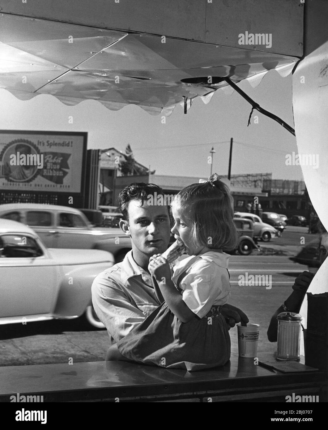 Ein kleines amerikanisches Mädchen, Helen Pennington, isst mit ihrem Vater einen Hot Dog am Fast-Food-Stand - undated Stockfoto