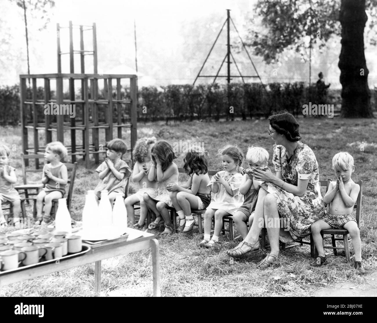 Die Kinder aus St. Leonard's Day Nursery sitzen in einer Reihe mit ihrem Kindergärtnermeister, um Gnade zu sagen, bevor sie ihre Milch am frühen Morgen trinken - 1946 Stockfoto