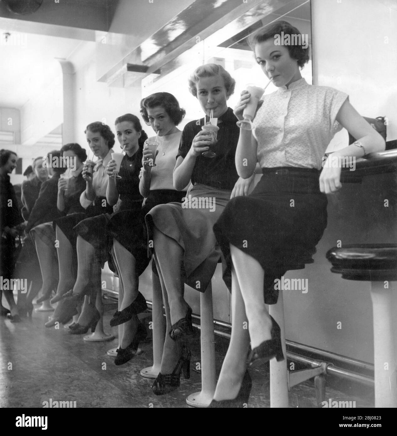 Junge Mädchen sitzen auf Hockern an der Theke mit einer Vielzahl von kalten Getränken an einer Milchbar in Leicester Square, London, England - 1951 Stockfoto