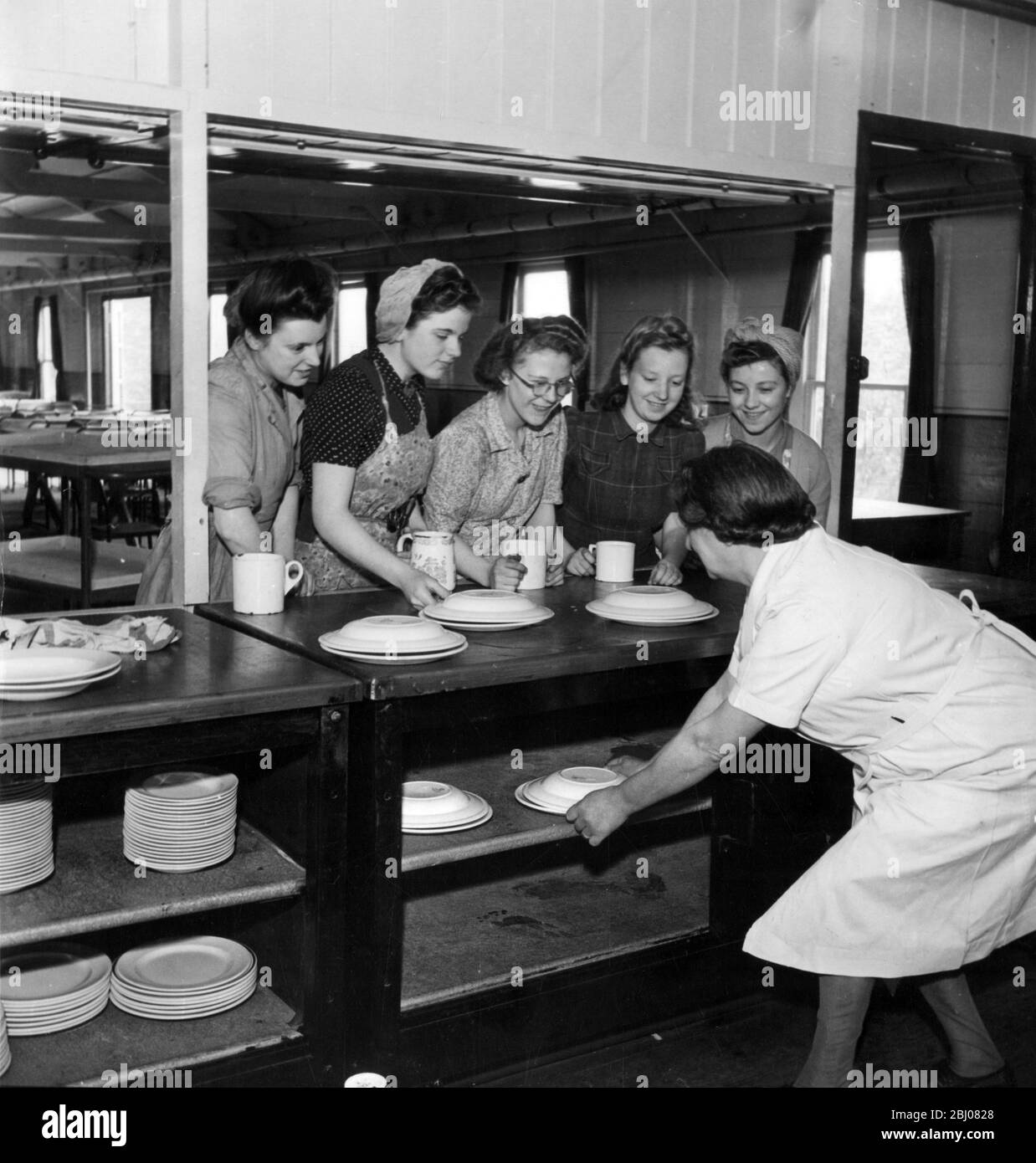 Mädchen, die ihr eigenes Abendessen mitgebracht haben, um im Ofen heiß zu bleiben, bis sie gebraucht werden, werden in der Ashton Brothers Cotton Mill Canteen, Hyde, Lancashire, England serviert. - 20. Oktober 1944 - Stockfoto