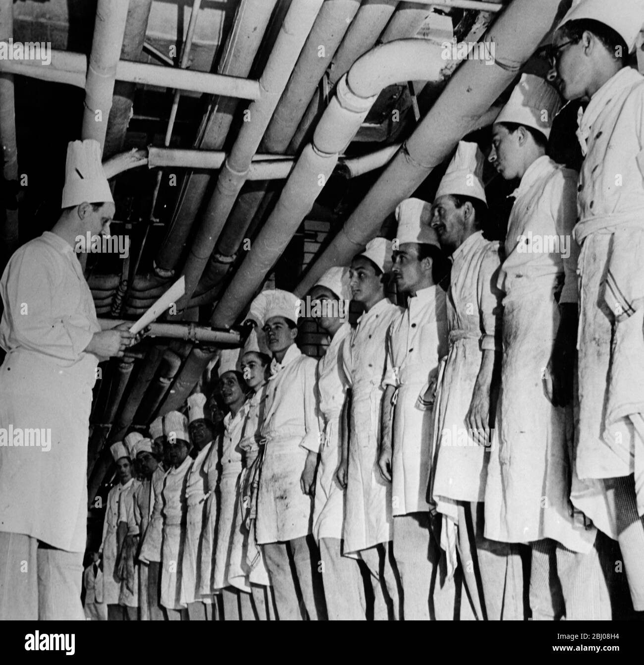 Lamouille, seit zehn Jahren Chefkoch des Ritz Hotels, liest den Küchenmitarbeitern die Tagesaufträge vor, während sie sich auf einen weiteren Tag kulinarischer Exzellenz vorbereiten. - 7. Oktober 1950 Stockfoto