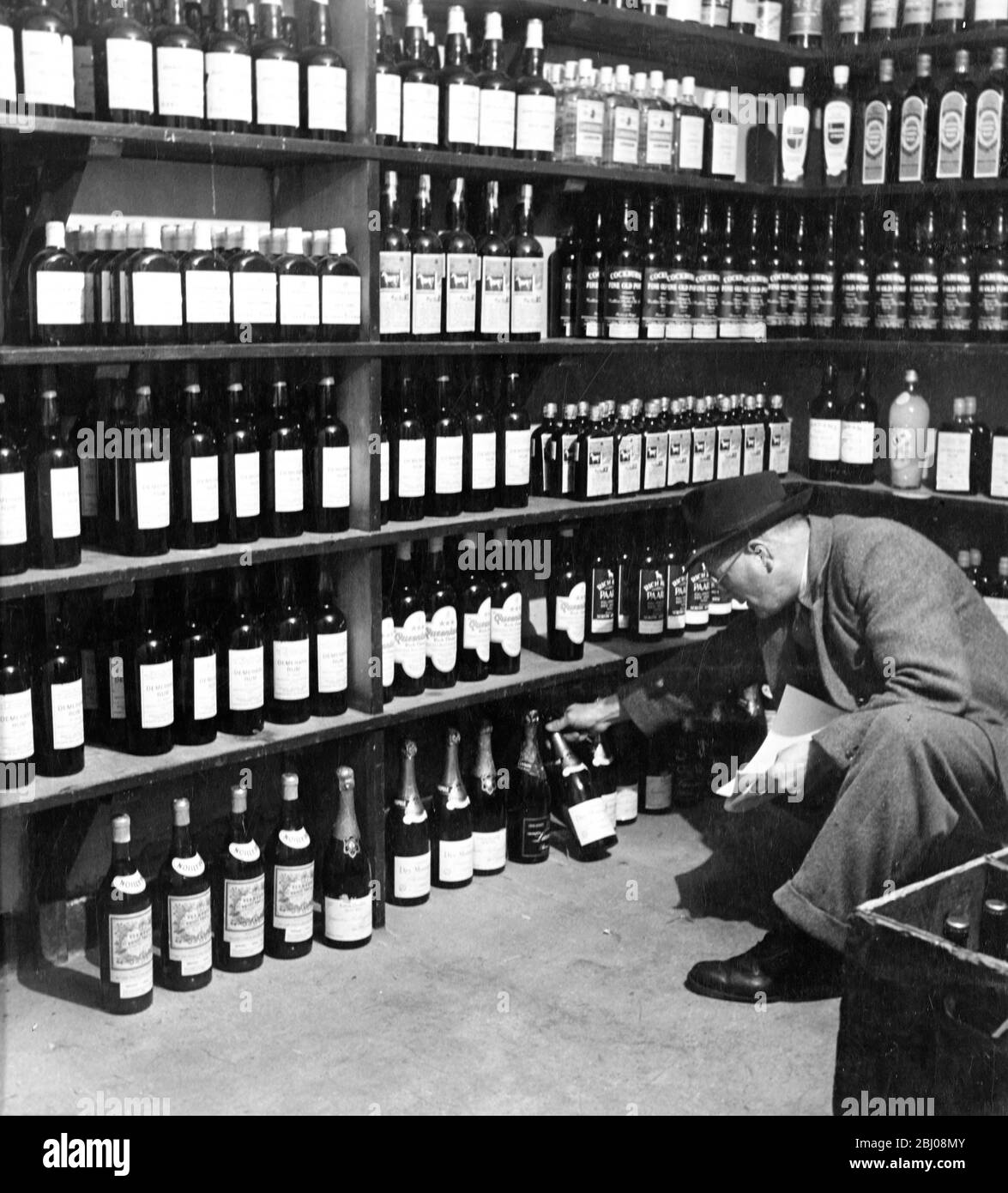 Mann, der in der Off-License-Abteilung der Globe Tavern durch die Weine und Spirituosen schaut. Ein Pub im Staatsbesitz in Longtown, Carlisle, Cumbria, England. - Dezember 1948 Stockfoto