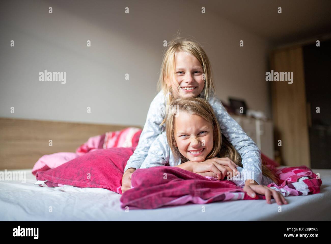 Zwei Mädchen liegen übereinander auf dem Bett und lächeln in die Kamera Stockfoto