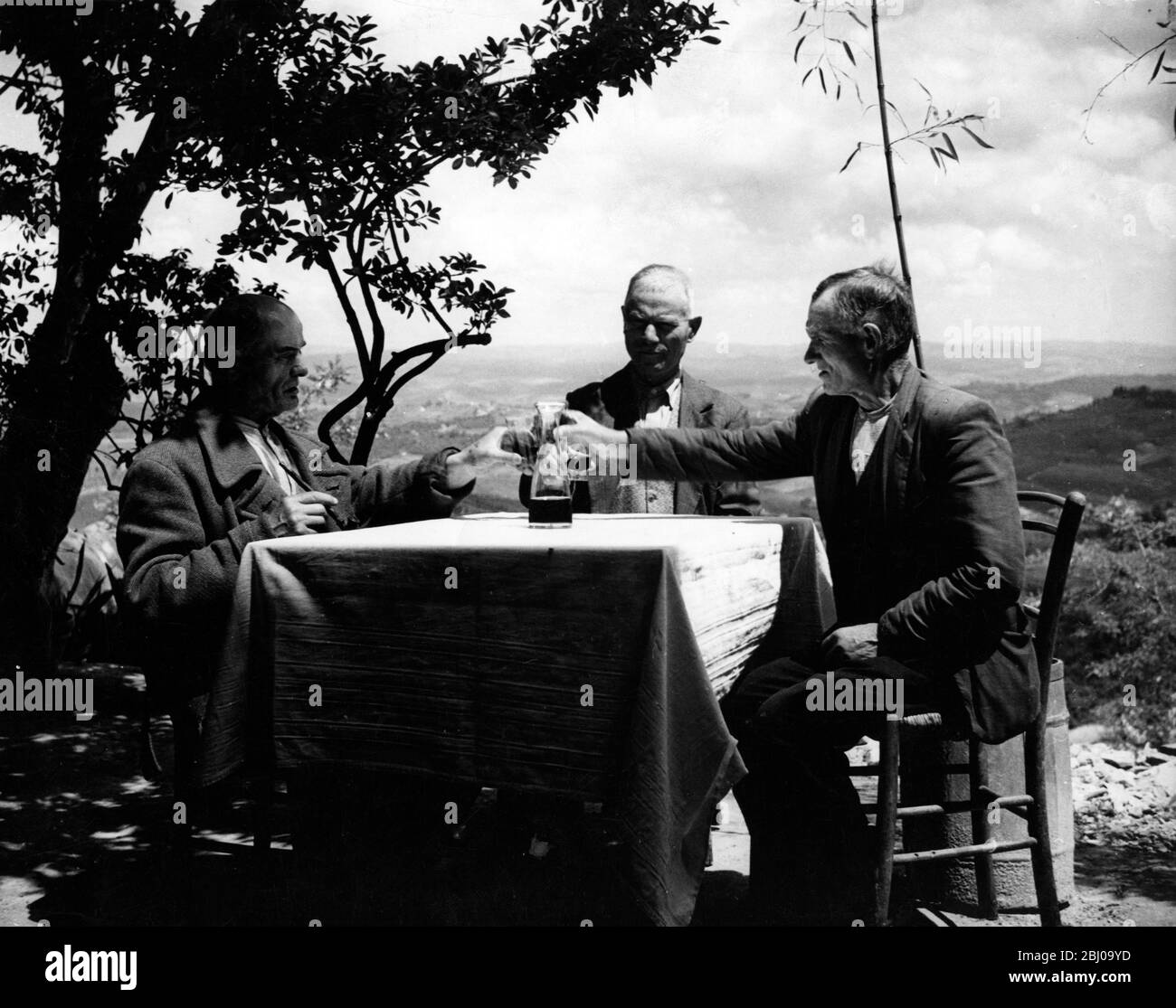 Drei Männer genießen Wein, während sie im Garten eines Gasthauses in Frascati, Italien sitzen - undated Stockfoto