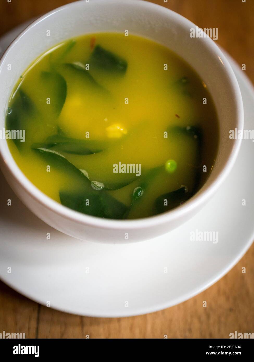 Leichte, frische Suppe aus Hummerbrühe mit Safran, Garnelen, Erbsen und Babyspinatblättern, serviert in einer großen Kaffeetasse. Stockfoto