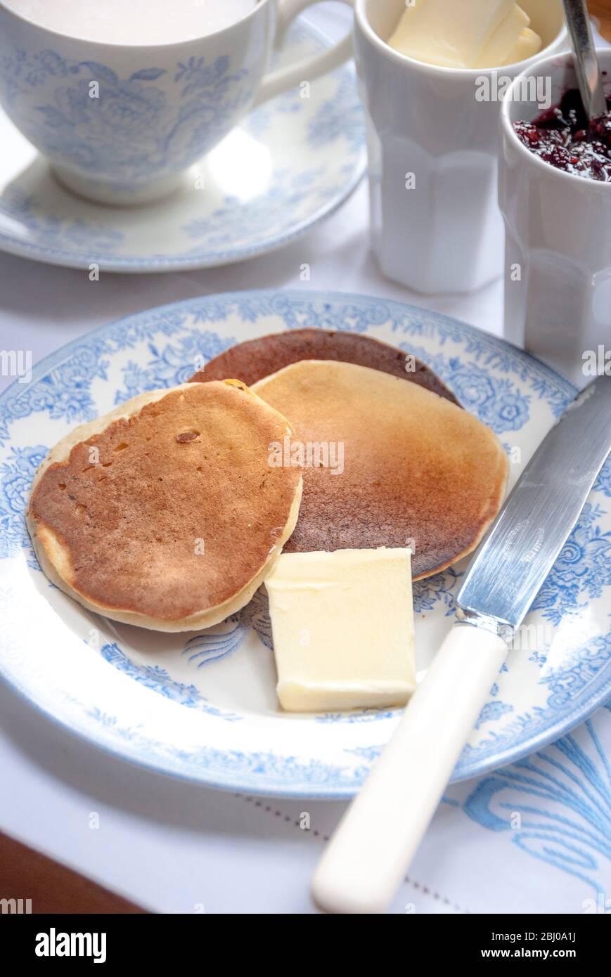 Hausgemachte Scotch Pancakes (Drop Scones) zum Teatime mit Butter und Himbeermarmelade und Tee. Stockfoto