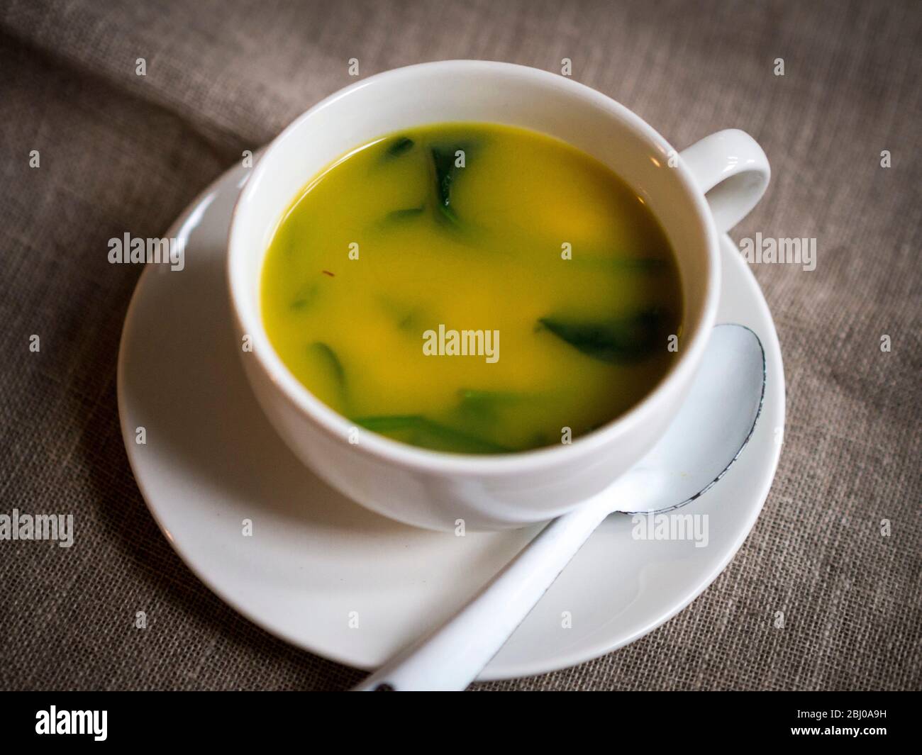 Leichte, frische Suppe aus Hummerbrühe mit Safran, Garnelen, Erbsen und Babyspinatblättern, serviert in einer großen Kaffeetasse. Stockfoto