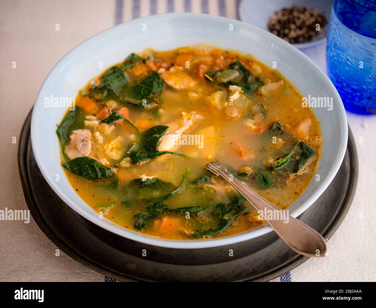 Komplette Mahlzeit Suppe von Huhn, Chorizo-Wurst und Gemüse mit braunem Reis, Linsen und Spinat, in blass blau Schüssel serviert Stockfoto